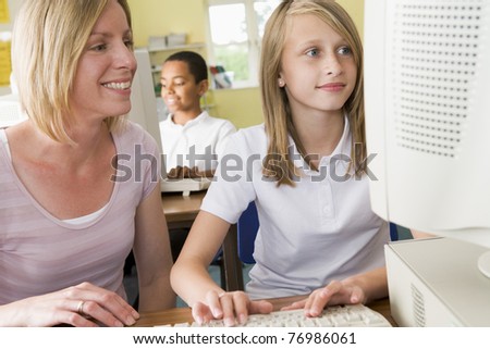 Student and teacher at computer terminal typing with student in background (selective focus)