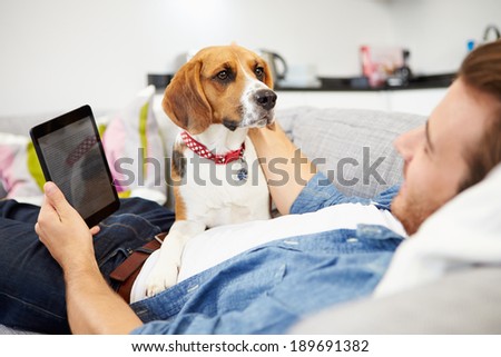 Young Man With Dog Sit On Sofa Using Digital Tablet