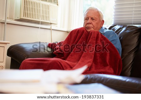 Senior Man Trying To Keep Warm Under Blanket At Home