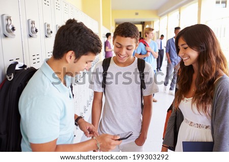 High School Students By Lockers Looking At Mobile Phone