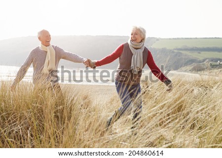 Senior Couple Walking Through Sand Dunes On Winter Beach - stock photo