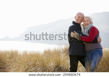 Senior Couple Walking Through Sand Dunes On Winter Beach
