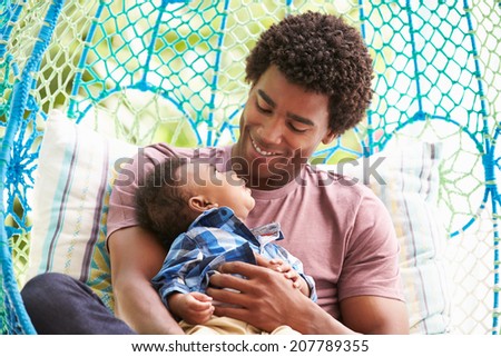 Father With Baby Son Relaxing On Outdoor Garden Swing Seat