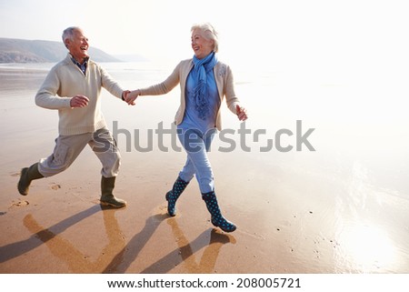 Senior Couple Running Along Winter Beach - stock photo