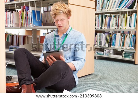 Male College Student Studying In Library With Digital Tablet