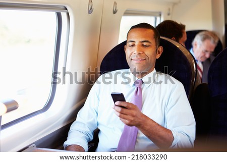 Businessman Commuting To Work On Train Using Mobile Phone