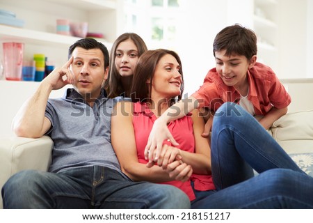 Hispanic Family Sitting On Sofa Watching TV Together