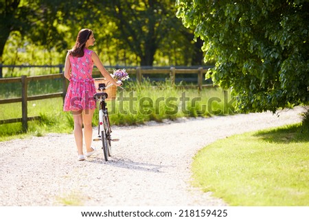 Rear View As Woman Pushes Bike Along Country Lane