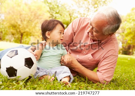 Grandfather And Grandson Playing With Football In Park