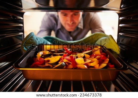 Man Putting Dish Of Vegetables Into Oven To Roast