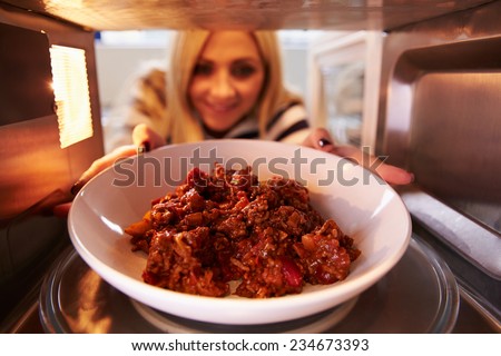 Woman Putting Leftover Chili Into Microwave Oven To Cook