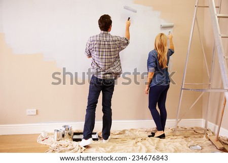 Couple Decorating Room Using Paint Rollers On Wall