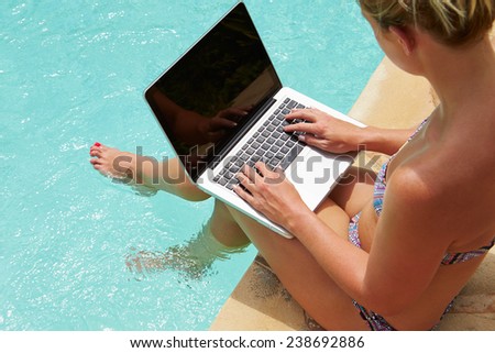 Woman Using Laptop Whilst Dangling Feet In Swimming Pool