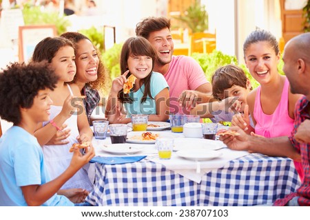 Two Families Eating Meal At Outdoor Restaurant Together