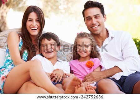 Portrait Of Family Sitting On Seat In Garden At Home