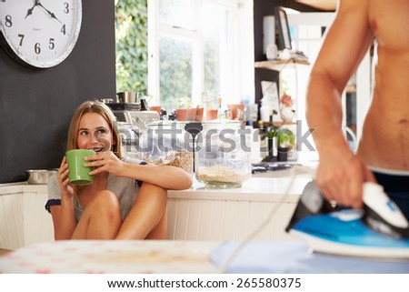 Woman Watching Man Ironing Shirt In Kitchen