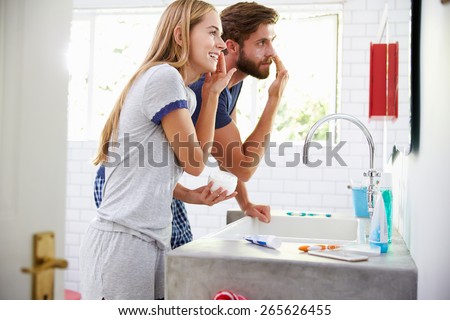 Couple In Pajamas Putting On Moisturizer In Bathroom