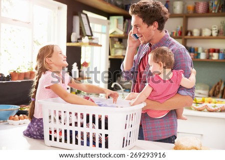 Father Using Mobile Phone As He Sorts Laundry With Children