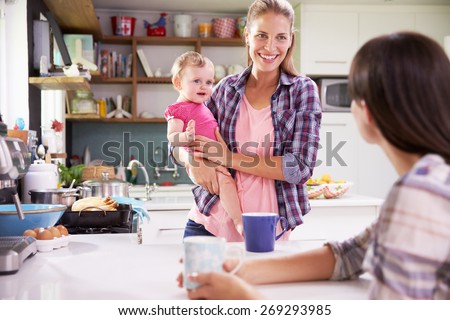 Mother With Young Daughter Talking To Friend In Kitchen