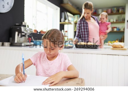 Girl Drawing Picture As Mother Prepares Meal In Kitchen
