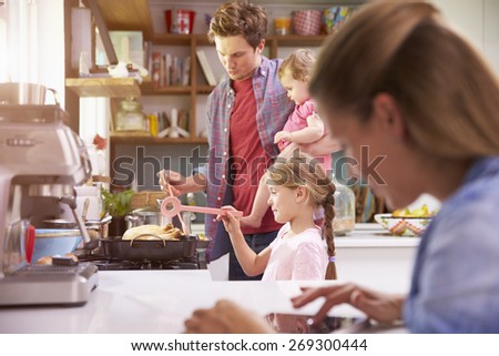 Father Cooks Family Meal Whilst Mother Uses Digital Tablet