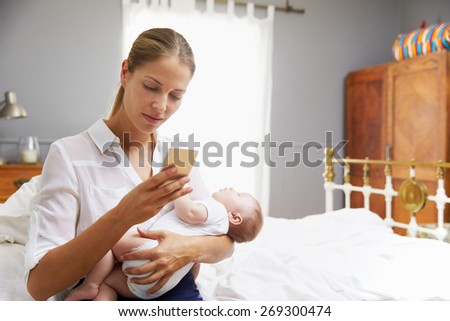 Working Mother Holding Baby And Checking Mobile Phone