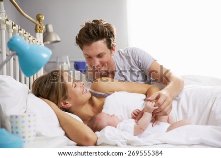 Family In Bed Holding Sleeping Newborn Baby Daughter