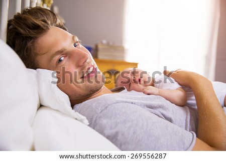 Father In Bed Holding Sleeping Newborn Baby Daughter