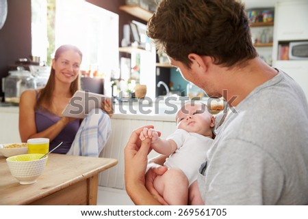 Family With Baby Girl Use Digital Tablet At Breakfast Table
