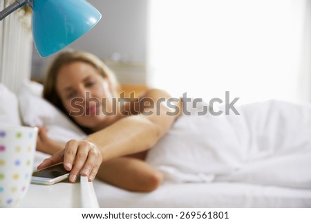 Woman Lying In Bed Reaching To Check Mobile Phone