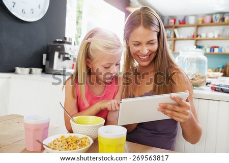 Mother And Daughter Using Digital Tablet At Breakfast Table