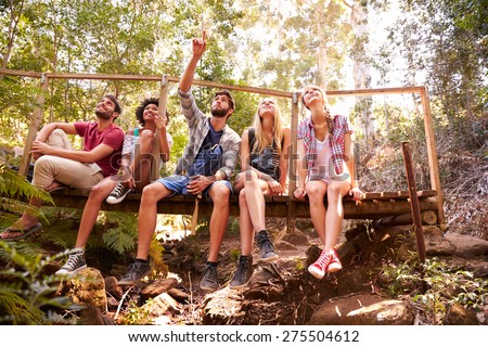 Group Of Friends On Walk Sitting On Wooden Bridge In Forest