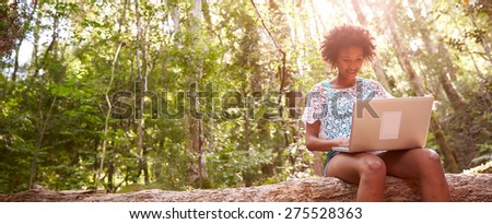 Woman Sits On Tree Trunk In Forest Using Laptop Computer