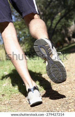 Close Up Of Man's Feet Jogging Along Woodland Path