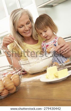Young Girl Helping Grandmother To Bake Cakes In Kitchen