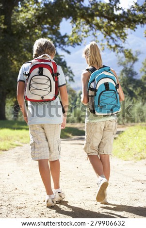 Teenage Couple Hiking Through Countryside Viewed From Back