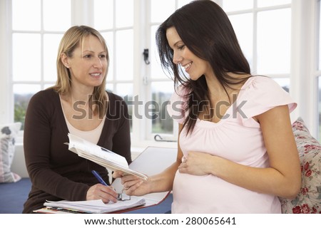 Pregnant Woman Reading Information Booklet At Home With Health Visitor