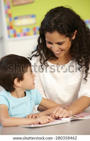 Elementary Age Schoolgirl Reading Book In Class With Teacher