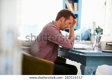 Stressed Man At Desk In Home Office With Laptop