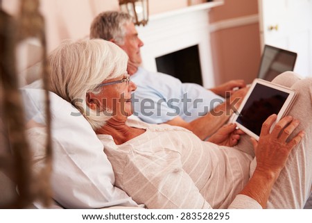 Senior Couple Lying In Bed Using Digital Devices