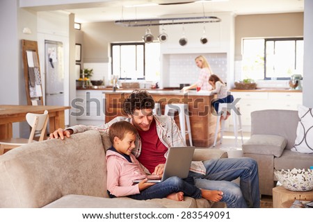 Father using computer with son, family in background