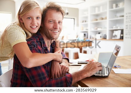 Girl hugging her father, working on laptop at home