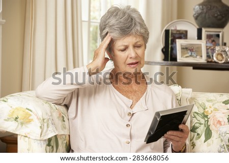 Unhappy Retired Senior Woman Sitting On Sofa At Home Looking At Photograph