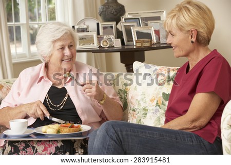 Helper Serving Senior Woman With Meal In Care Home
