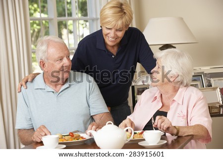 Senior Couple Enjoying Meal Together At Home With Home Help