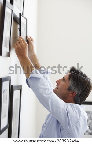 Man Hanging Picture Frames On Wall At Home