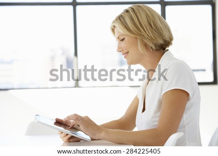 Businesswoman Sitting At Desk In Office Using Digital Tablet