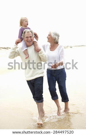 Grandparents And Granddaughter Walking Along Beach Together