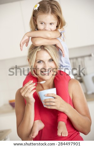 Daughter Sitting On Shoulders Whilst Mother Eats Yoghurt