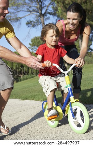Parents Teaching Son To Ride Bike In Park